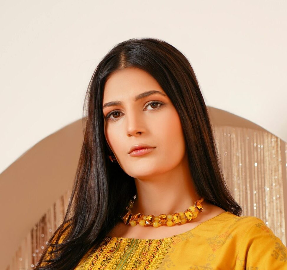 A stylish young woman in traditional yellow attire posing elegantly indoors.